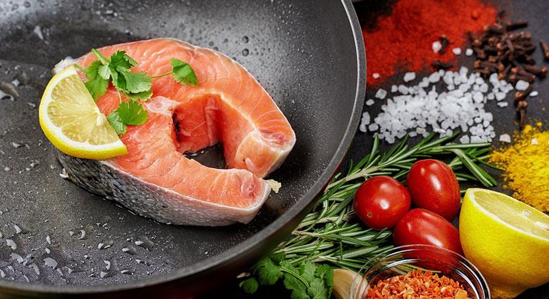 鲑鱼排在铸铁煎锅里，周围环绕着蔬菜 